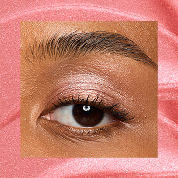 Close-up of an eye area with NYX Professional Makeup Lid Lingerie Cream Eye Pigment in 04 Risky Rose, shown on a rose gold shimmer textured background.