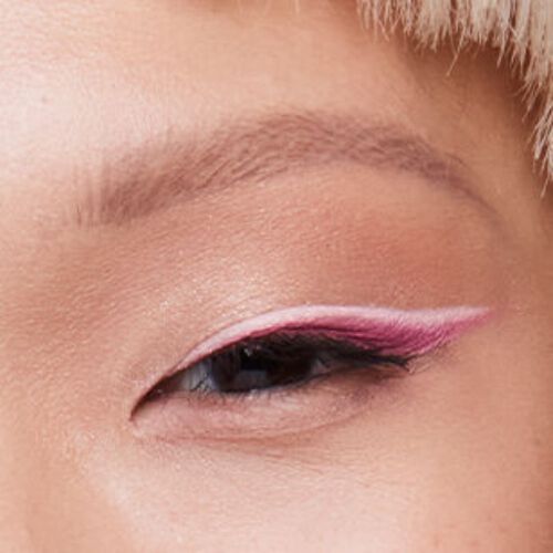 A close-up shot of a woman’s eye with pink winged eyeliner and skinny brows.